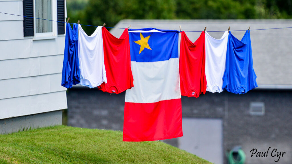An Acadian flag on a clothesline with red, white and blue clothing