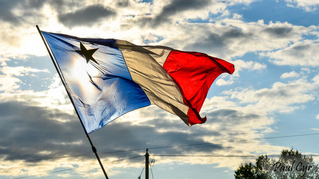 Acadian flag flying with the sun shining through it